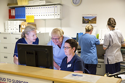 clinical professionals in a ward reception area gathered around a computer monitor