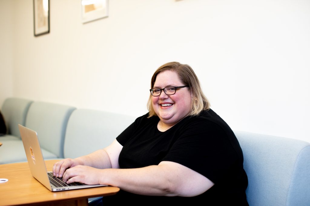 A person sitting down whilst using a laptop, smiling.